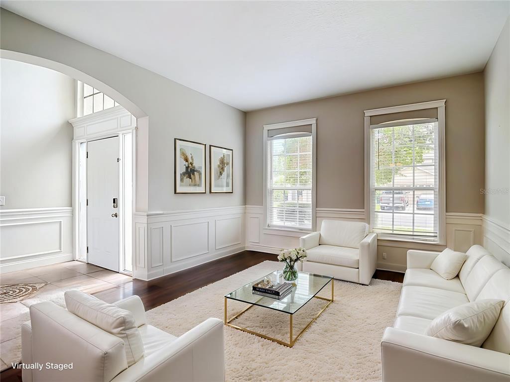 A living room with white wainscoting, white furniture, a glass coffee table, and two windows — 10739 EVENINGWOOD COURT, TRINITY, FL