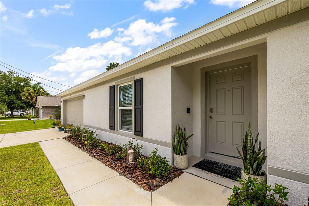 A light-colored house exterior features a front door, a window with shutters, and landscaping — 49 LLAMA TRAIL, PALM COAST, FL
