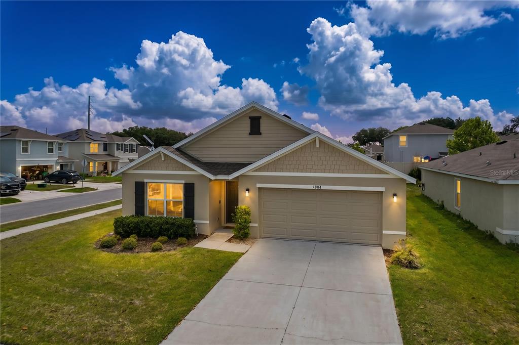 A tan single-story suburban house features a two-car garage and a front yard lawn — 7804 DAVIE RAY DRIVE, ZEPHYRHILLS, FL