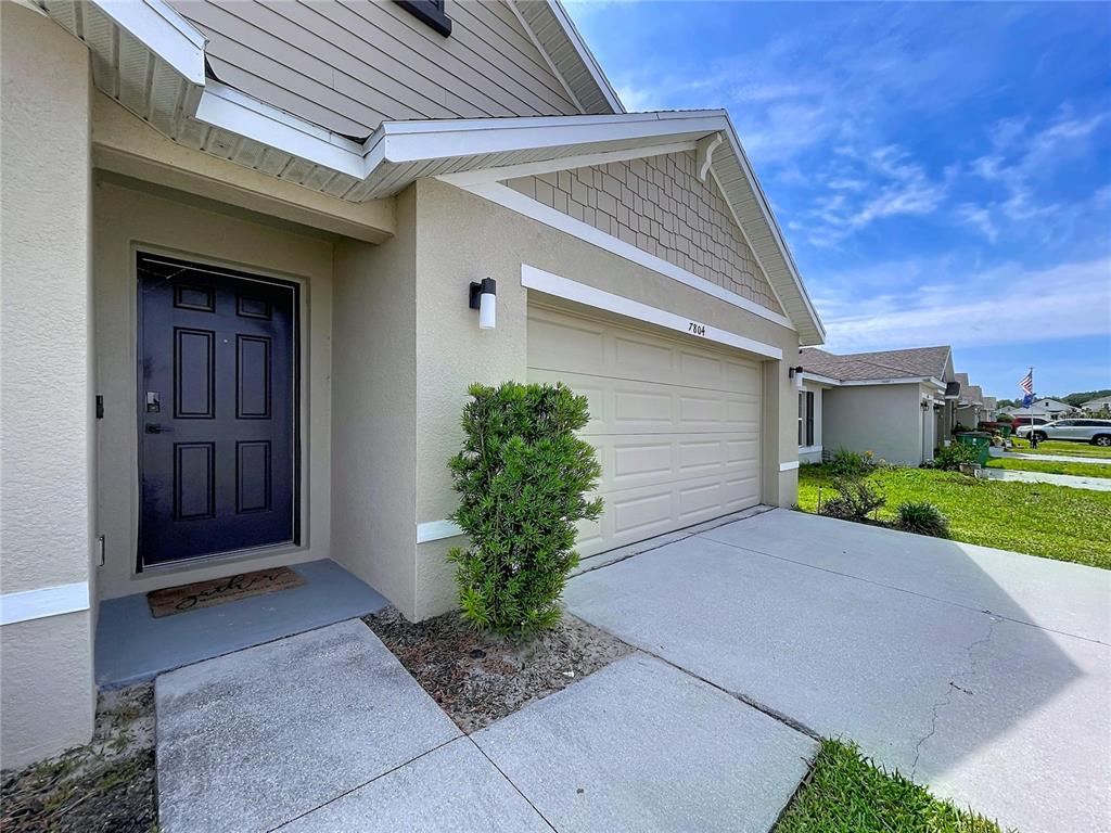 A beige house exterior features a dark front door, a garage, and a concrete walkway — 7804 DAVIE RAY DRIVE, ZEPHYRHILLS, FL