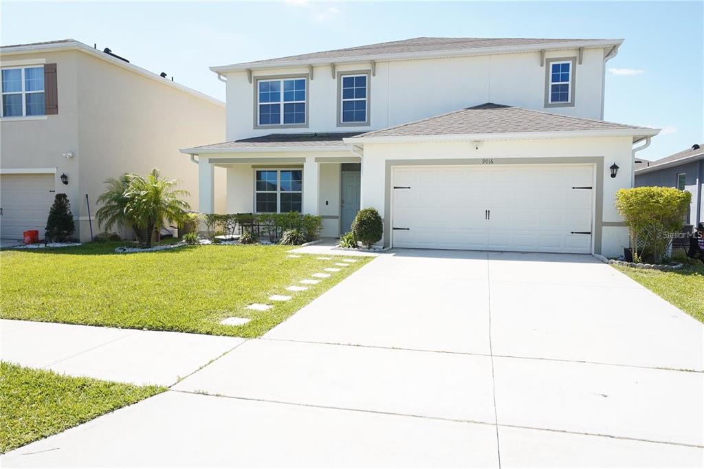 A two-story suburban house with a white stucco exterior, a two-car garage, and a driveway — 9016 PYRUS STREET, KISSIMMEE, FL