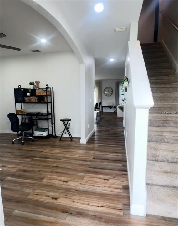 A room with wood-look flooring features a desk area, a staircase, and an arched entryway — 9016 PYRUS STREET, KISSIMMEE, FL