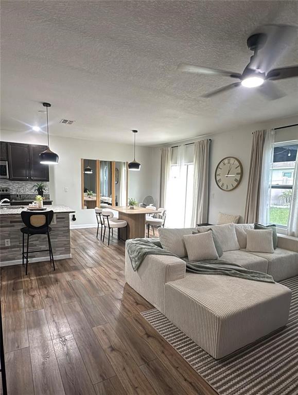 An open-concept living and dining area features wood-look flooring, a kitchen island, and a sectional — 9016 PYRUS STREET, KISSIMMEE, FL