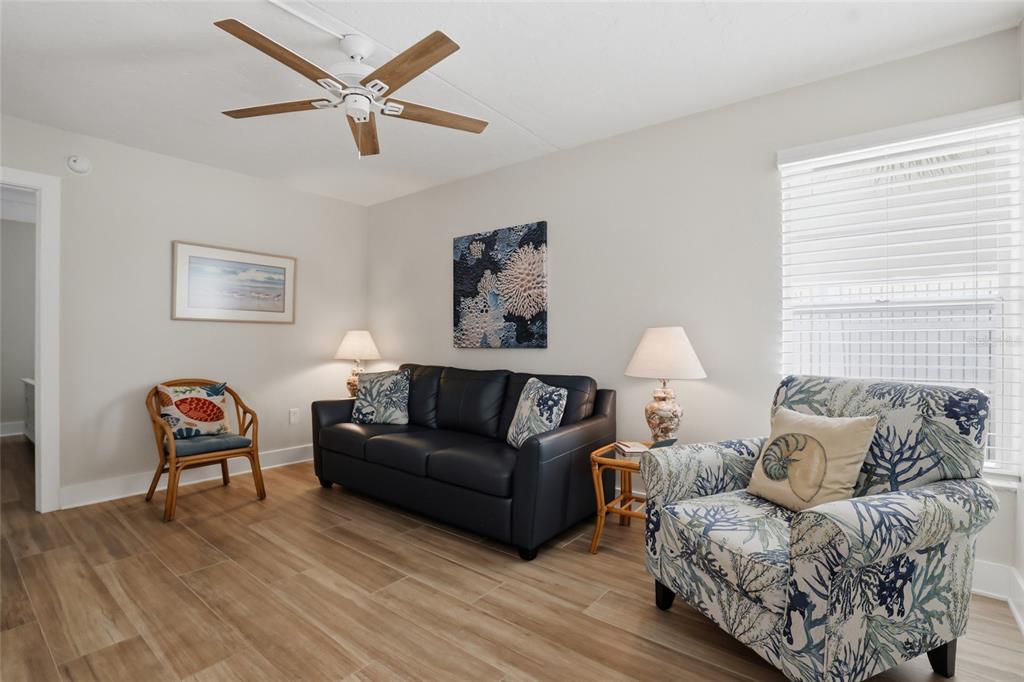 A living room features a dark leather sofa, a patterned armchair, and wood-look tile flooring — 5950 MIDNIGHT PASS ROAD UNIT 101, SARASOTA, FL