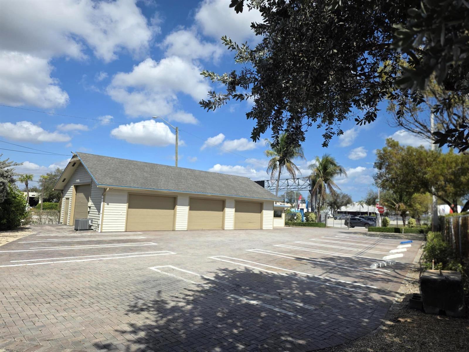 A beige garage building with three roll-up doors sits on a paved parking lot — 1710 W Atlantic Avenue, Delray Beach FL 33444, DELRAY BEACH, FL