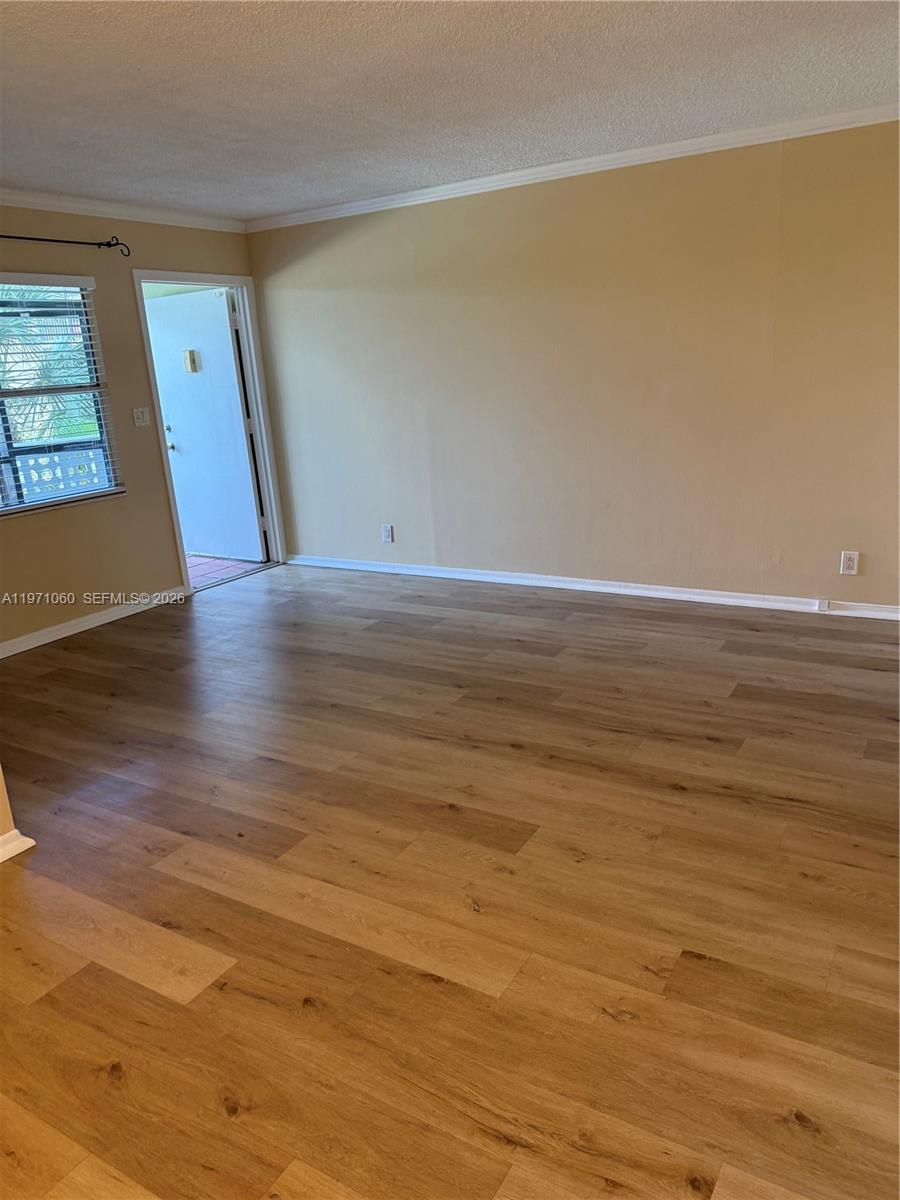 An empty room features light wood-look flooring, beige walls, and a door leading outside — 1425 Arthur St # 315B, Hollywood FL 33020, HOLLYWOOD, FL
