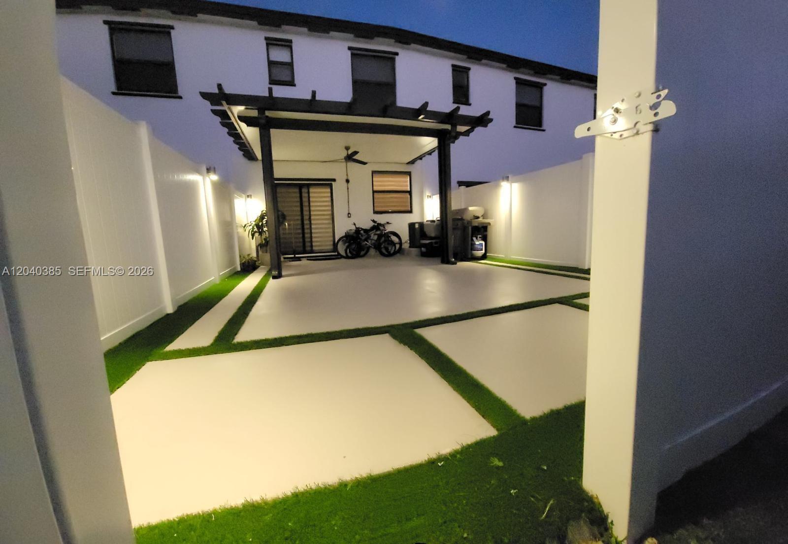A paved patio area features a pergola, artificial turf accents, and white privacy fencing — 11038 W 32nd Ln # 11038, Hialeah FL 33018, HIALEAH, FL