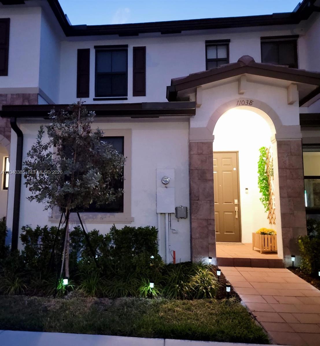 A two-story house exterior features a stone-arched entryway, a brown door, and landscape lighting — 11038 W 32nd Ln # 11038, Hialeah FL 33018, HIALEAH, FL