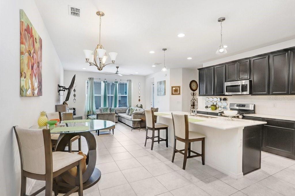 An open-concept kitchen and dining area features dark cabinets, a white island, and tile flooring — 6321 CAMINO DRIVE, APOLLO BEACH, FL