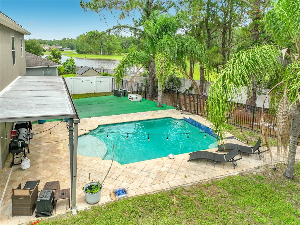 An elevated view of a backyard featuring a swimming pool, patio, and green turf area — 10672 CABBAGE TREE LOOP, ORLANDO, FL