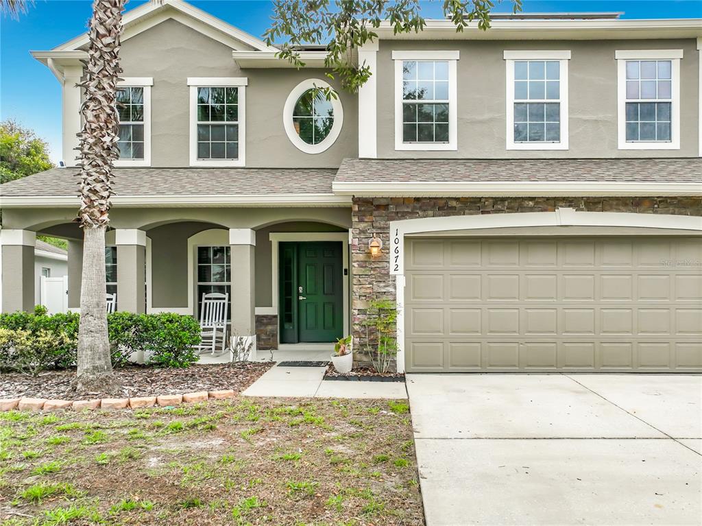 A two-story house with a beige stucco exterior, a stone-accented garage, and a green front door — 10672 CABBAGE TREE LOOP, ORLANDO, FL