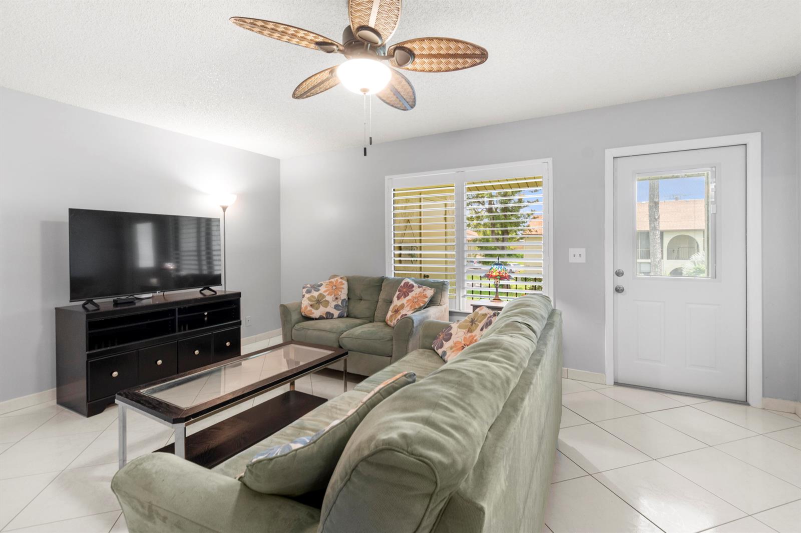 A living room features green sofas, a glass coffee table, a television, and tile flooring — 317 Knotty Pine Circle # 2, FL 33463, FL