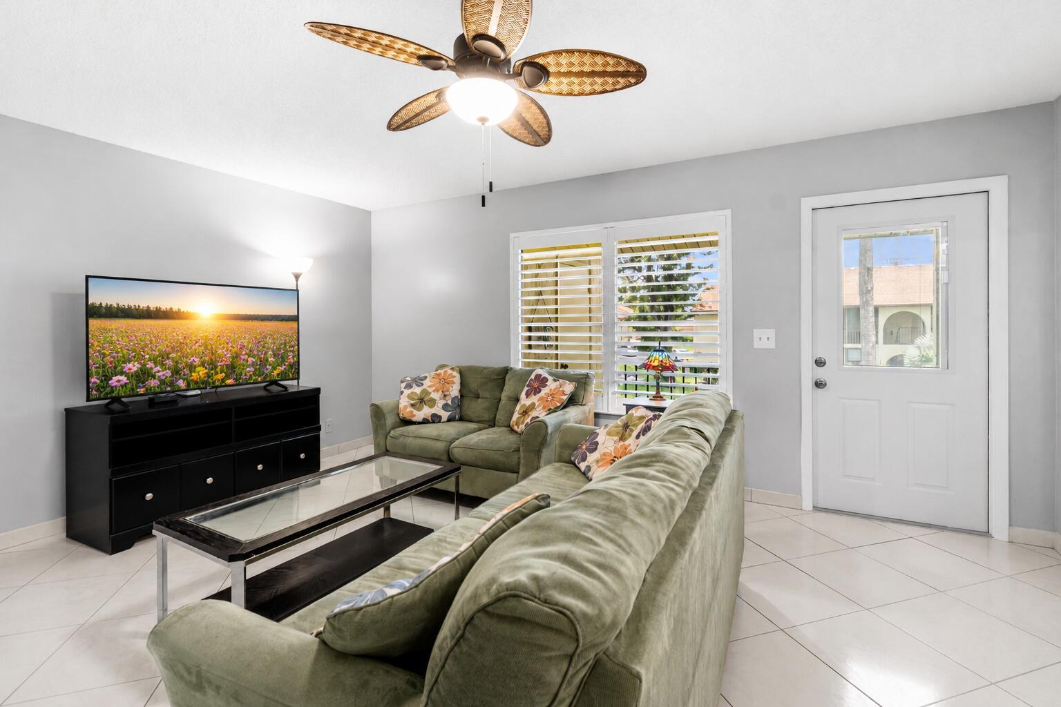 A living room features a green sofa and loveseat, a glass coffee table, and television — 317 Knotty Pine Circle # 2, FL 33463, FL