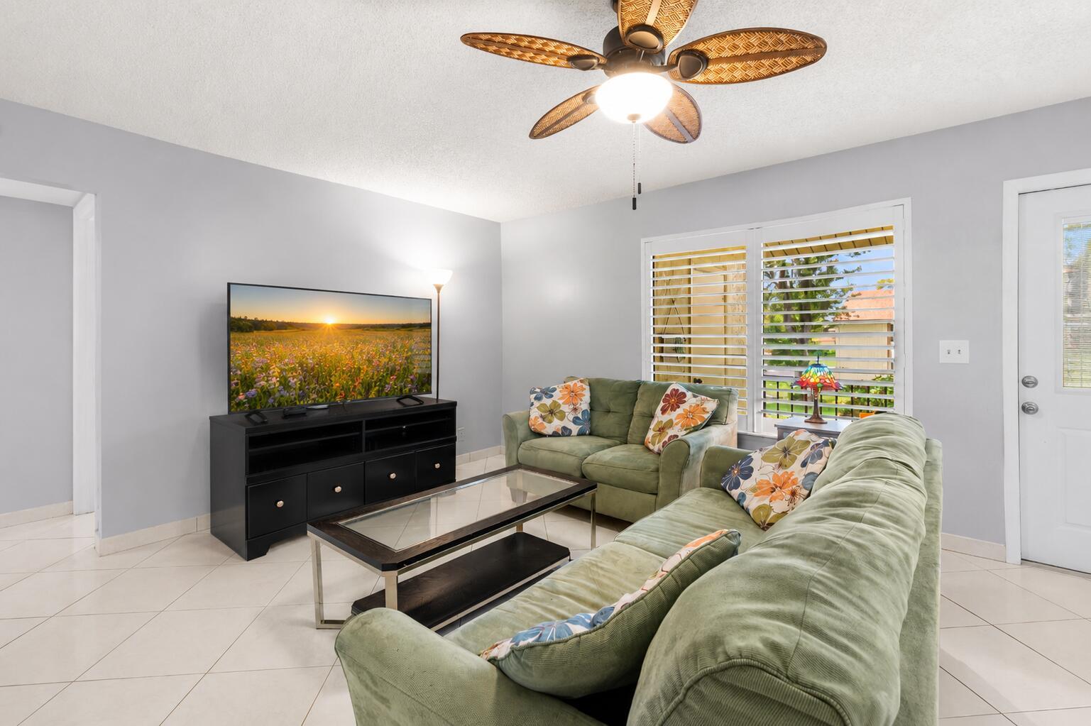 A living room features two sage green sofas, a glass-top coffee table, and a ceiling fan — 317 Knotty Pine Circle # 2, FL 33463, FL
