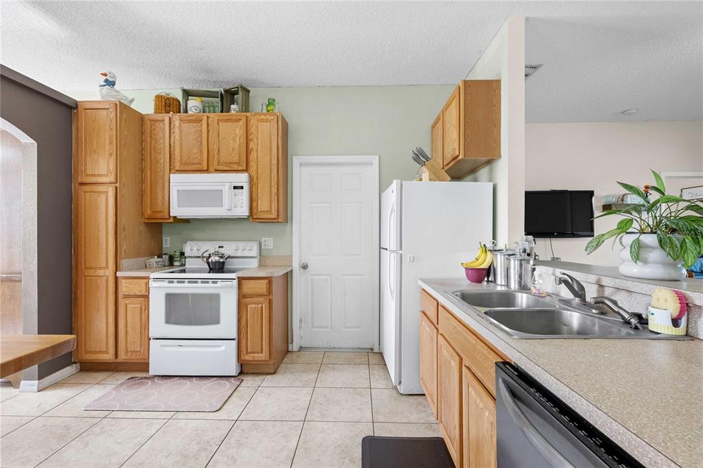 A kitchen features light wood cabinets, white appliances, a double sink, and tiled flooring — 2420 SE 75TH BOULEVARD, BUSHNELL, FL