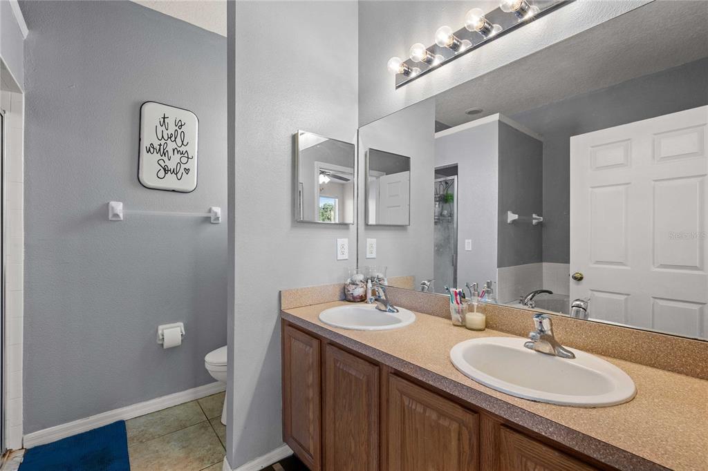 A bathroom features a double vanity with a beige countertop, wood cabinets, and a large mirror — 2420 SE 75TH BOULEVARD, BUSHNELL, FL