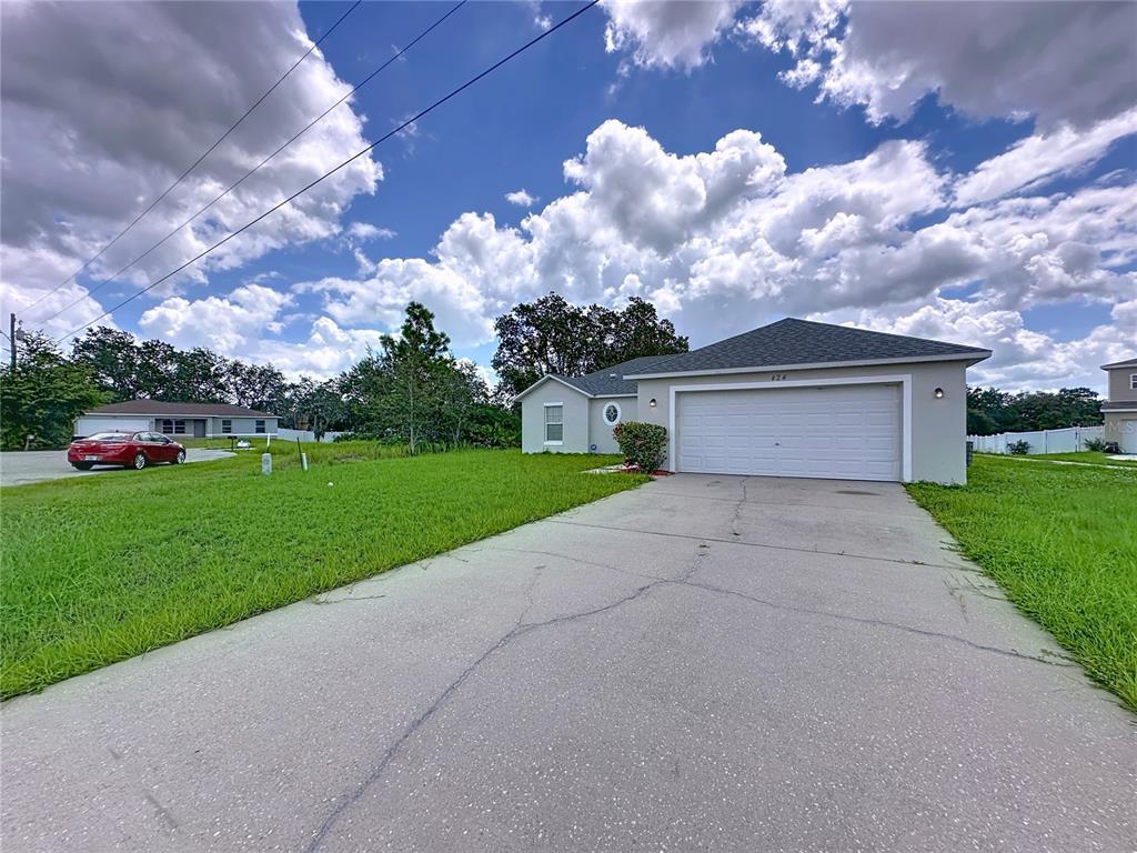 A single-story house with a white garage door and a concrete driveway under a cloudy sky — 424 DANUBE WAY, KISSIMMEE, FL