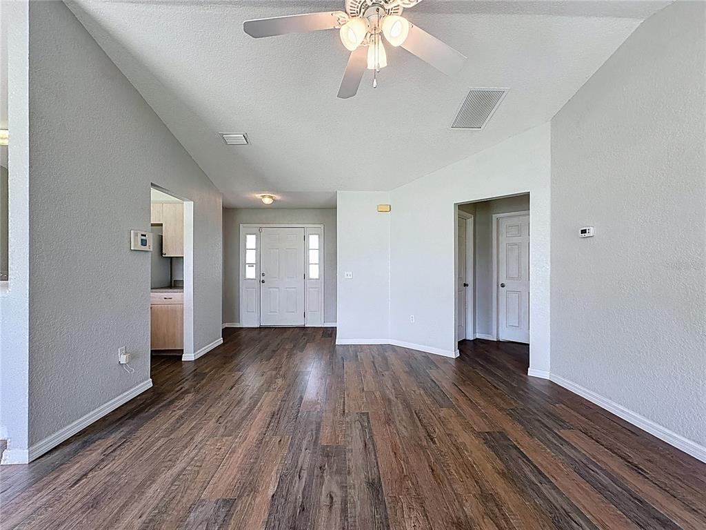 An interior view of a living room with wood-look flooring, a ceiling fan, and doorways — 424 DANUBE WAY, KISSIMMEE, FL
