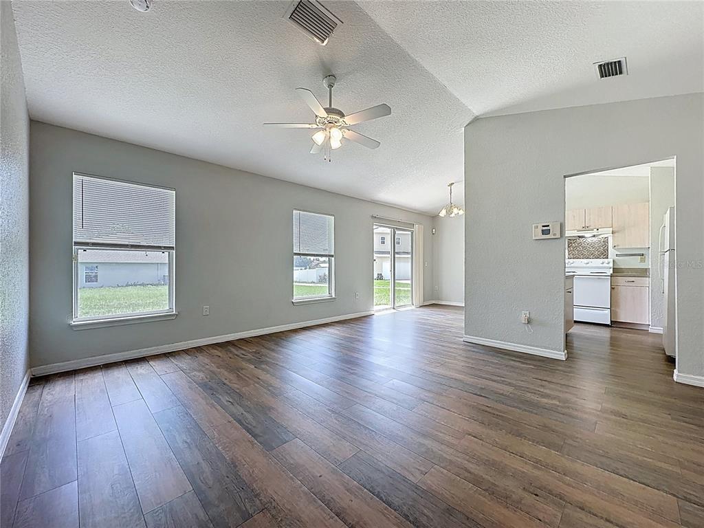 An open living area features wood-look flooring, a ceiling fan, and an adjacent kitchen — 424 DANUBE WAY, KISSIMMEE, FL