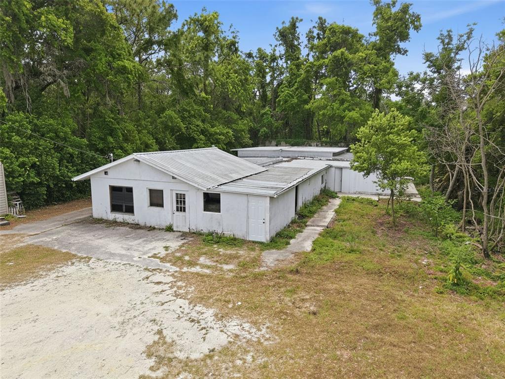 An exterior view of a white, single-story building with a metal roof and surrounding trees — 15520 CORTEZ BOULEVARD, BROOKSVILLE, FL