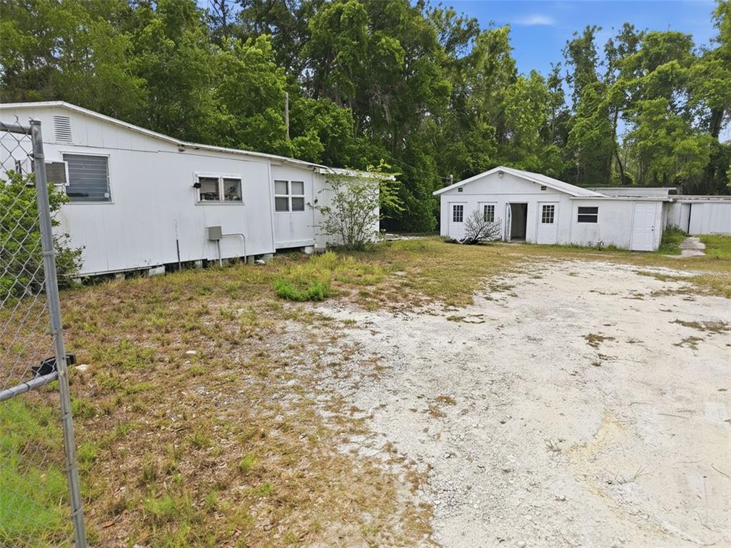 Two white, single-story buildings sit on a gravel lot surrounded by trees and a fence — 15520 CORTEZ BOULEVARD, BROOKSVILLE, FL