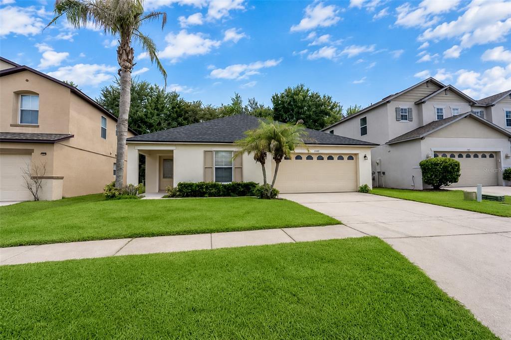 A single-story suburban house with a tan exterior, a two-car garage, and a palm tree — 1503 BLUE HORIZON DRIVE, CLERMONT, FL