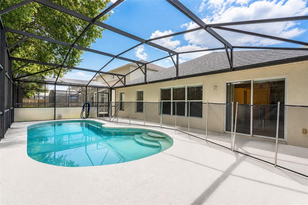A screened-in patio features a swimming pool with a safety fence and sliding glass doors — 1503 BLUE HORIZON DRIVE, CLERMONT, FL