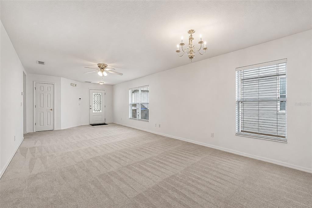 An empty living room features beige carpeting, white walls, a ceiling fan, and a chandelier — 1503 BLUE HORIZON DRIVE, CLERMONT, FL