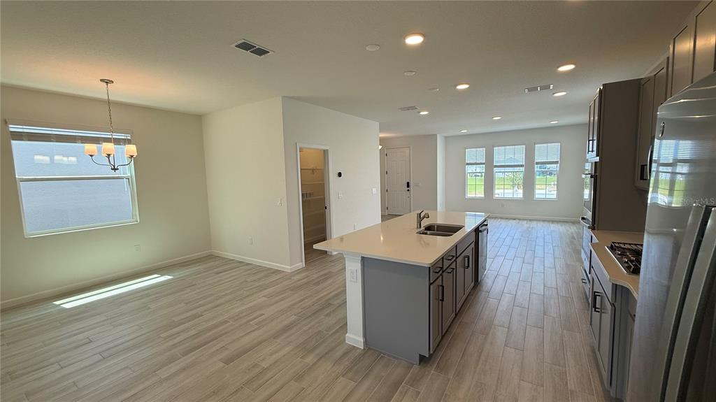 A kitchen with a gray island and light wood-look flooring opens to a dining area — 17125 BEACHGRASS ALLEY, WINTER GARDEN, FL