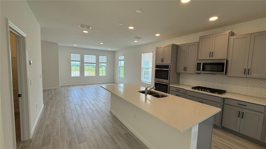 A modern kitchen features gray cabinets, a large island with a sink, and tile flooring — 17125 BEACHGRASS ALLEY, WINTER GARDEN, FL