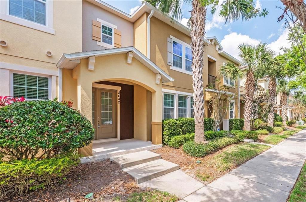 A tan two-story townhouse exterior features a covered entryway, palm trees, and a concrete sidewalk — 8642 VIA TAVOLERIA WAY, WINDERMERE, FL