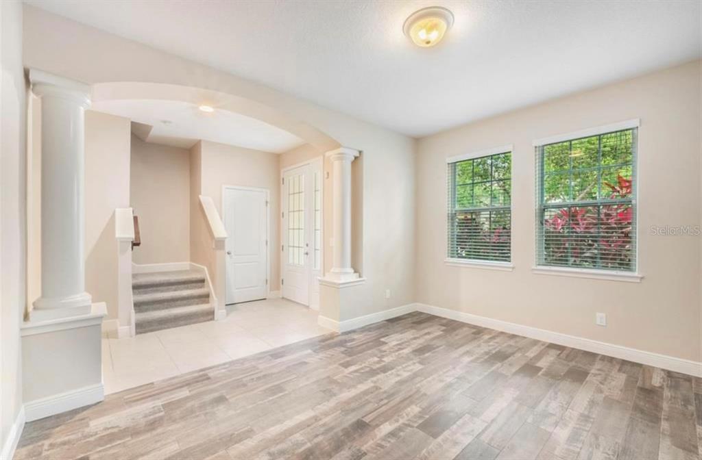 A room with wood-look flooring, an arched entryway with columns, and a carpeted staircase — 8642 VIA TAVOLERIA WAY, WINDERMERE, FL