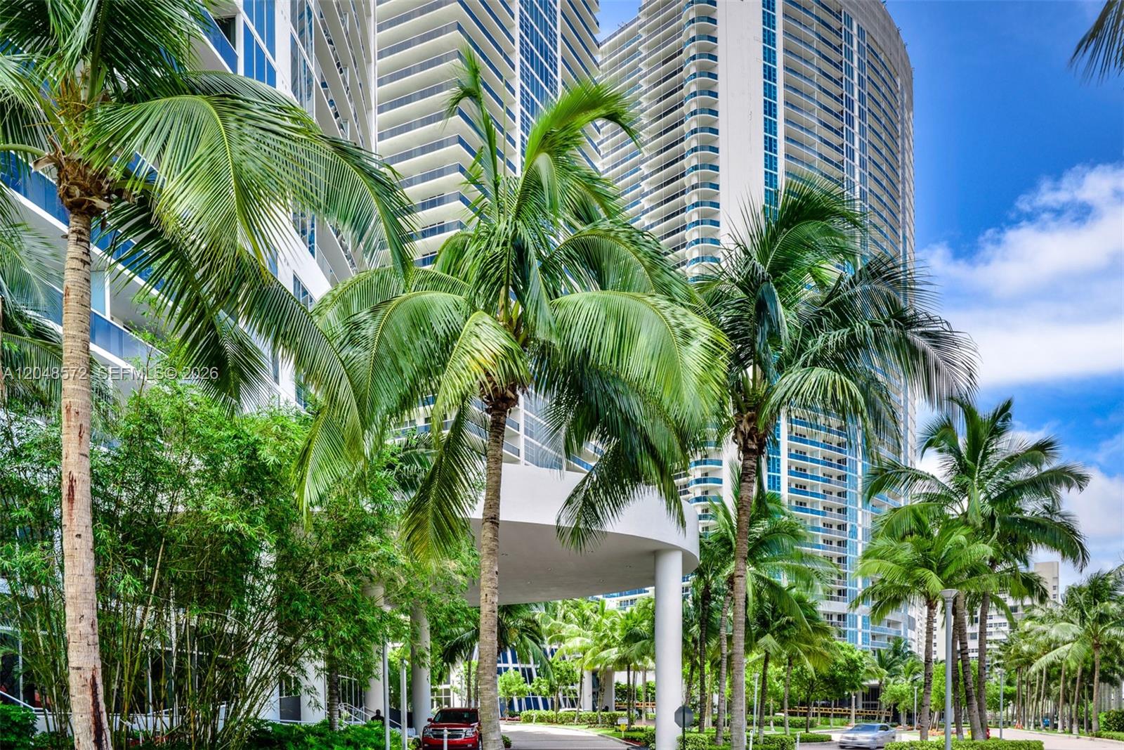 A low-angle view of tall modern residential towers surrounded by lush palm trees and greenery — 1800 S Ocean Dr # 2203, Hallandale Beach FL 33009, HALLANDALE BEACH, FL