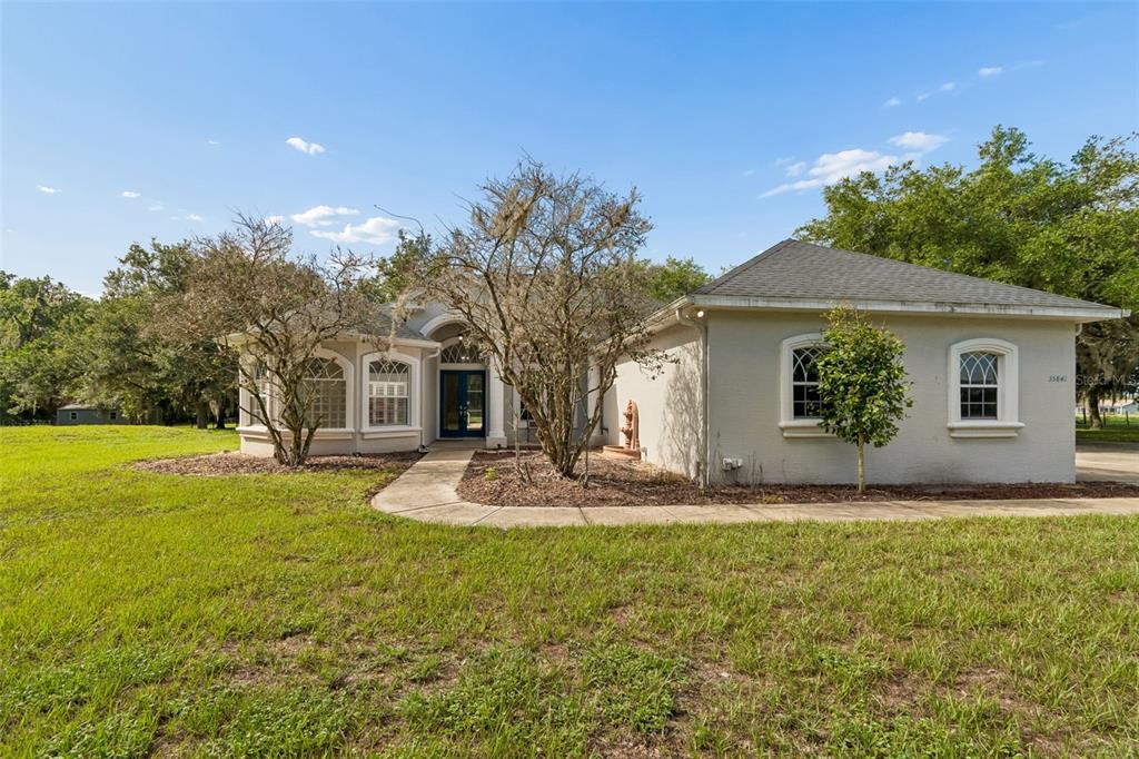 A single-story house with a light-colored stucco exterior, arched windows, and a front walkway — 35841 MIDDEN PATH, ZEPHYRHILLS, FL