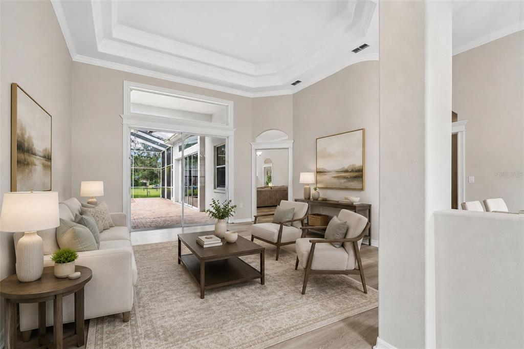 A bright living room features a tray ceiling, neutral furniture, and sliding glass doors to a patio — 35841 MIDDEN PATH, ZEPHYRHILLS, FL
