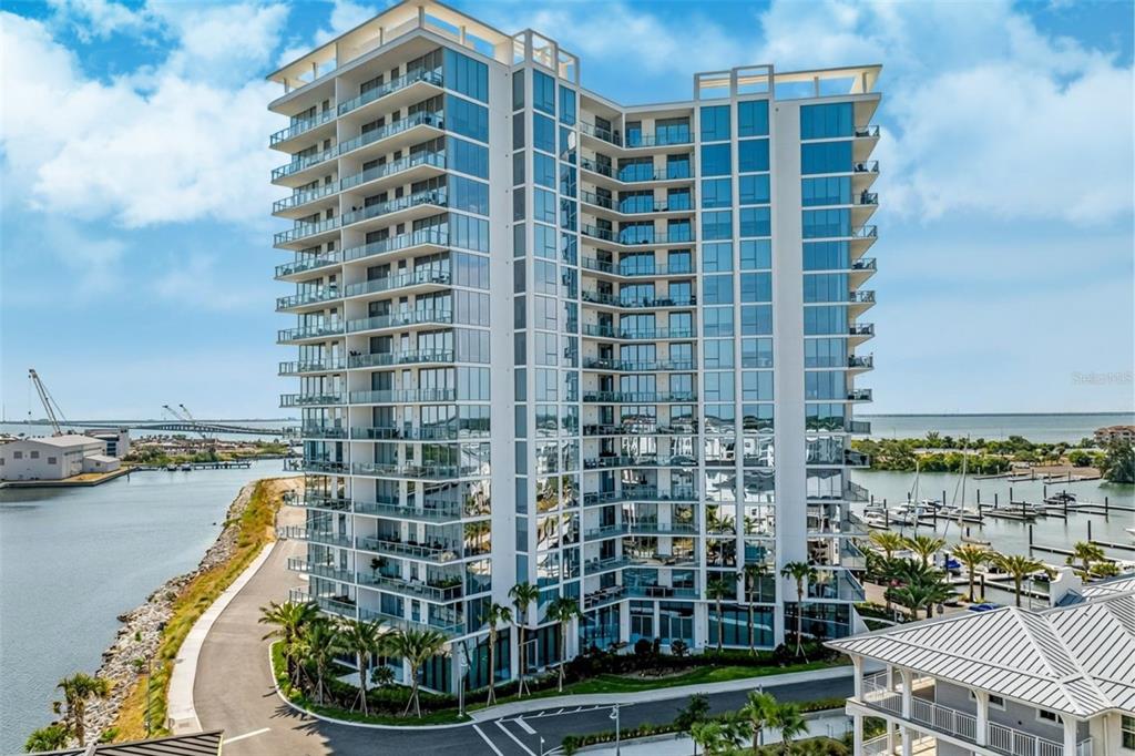 An aerial view of a modern high-rise condominium building situated next to a marina — 5120 MARINA WAY UNIT 9907, TAMPA, FL
