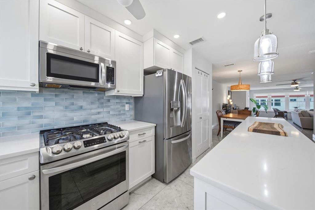A modern kitchen features white cabinets, stainless steel appliances, and a light blue tiled backsplash — 3018 59TH STREET S UNIT 414, GULFPORT, FL