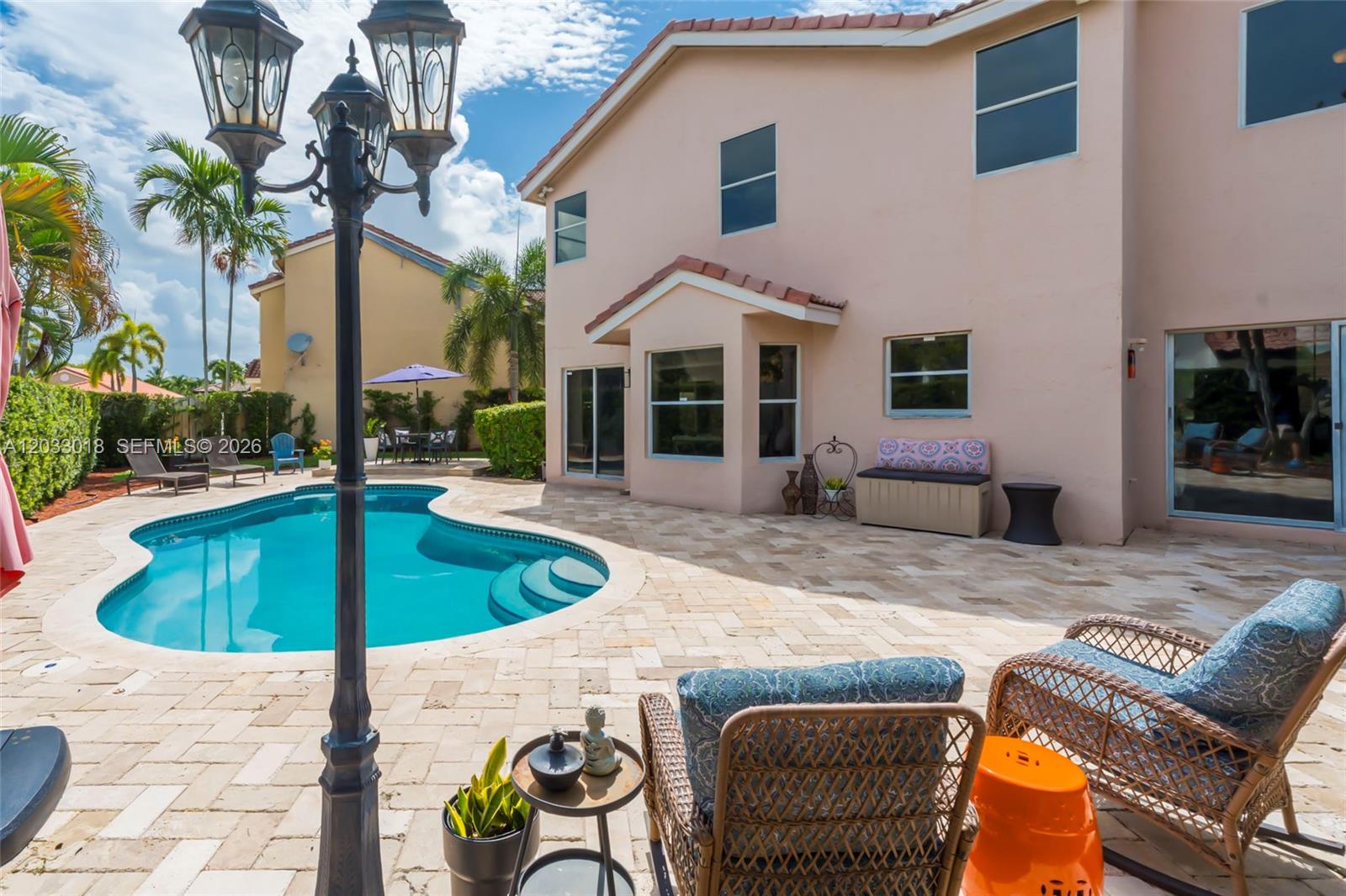 A backyard patio features a swimming pool, wicker chairs, and a two-story peach-colored house — 18172 SW 3rd St, Pembroke Pines FL 33029, PEMBROKE PINES, FL