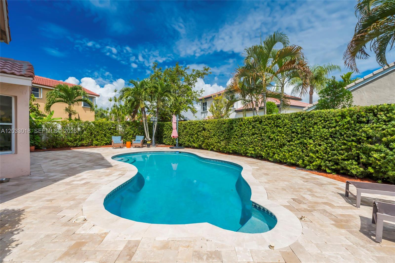 A backyard features a kidney-shaped swimming pool surrounded by stone pavers and a tall hedge — 18172 SW 3rd St, Pembroke Pines FL 33029, PEMBROKE PINES, FL