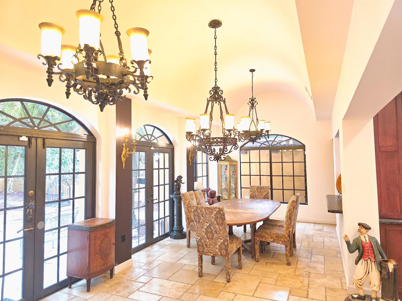 A dining room features a wooden table, patterned chairs, two chandeliers, and arched glass doors — 4200 N Surf Road, Hollywood FL 33019, HOLLYWOOD, FL