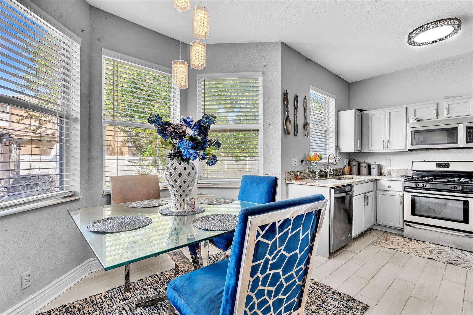 A dining area with a glass table and blue chairs sits next to a white kitchen — 5743 Raceway Road, Lake Worth FL 33449, LAKE WORTH, FL