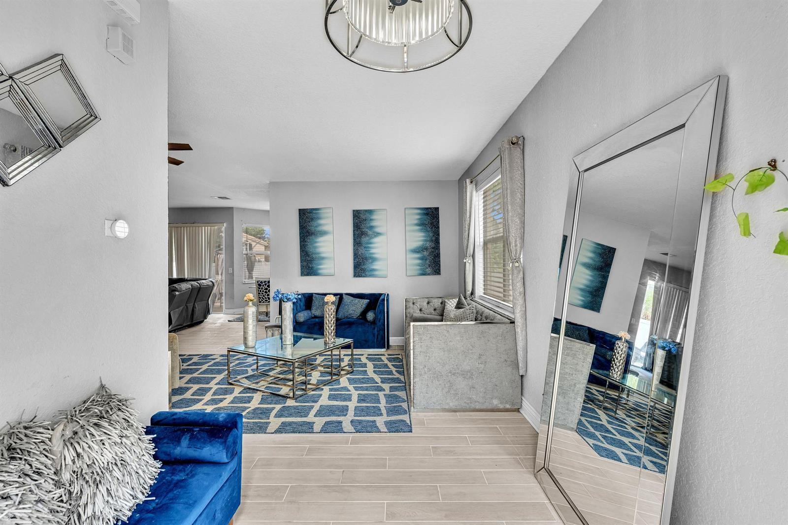 A living room features a blue sofa, a glass coffee table, and a large floor mirror — 5743 Raceway Road, Lake Worth FL 33449, LAKE WORTH, FL