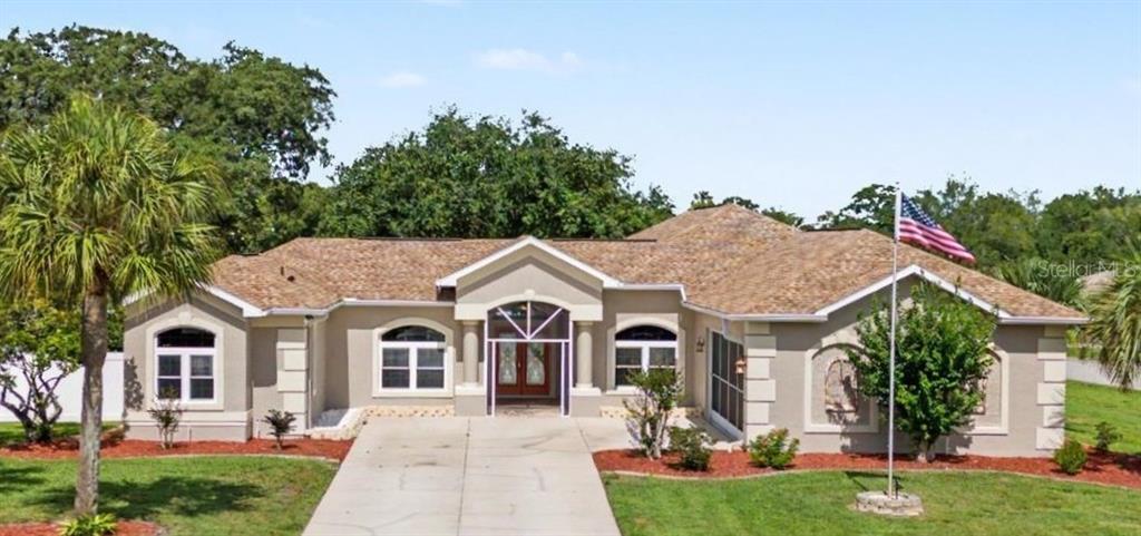 A single-story house with a beige stucco exterior, a shingled roof, and a concrete driveway — 10339 BEDFORD ROAD, SPRING HILL, FL
