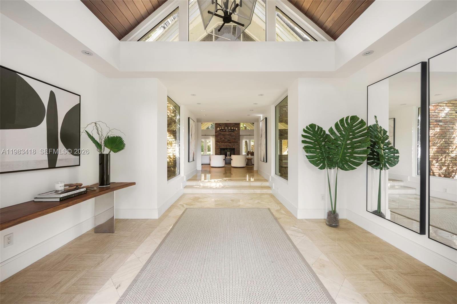 A bright, modern foyer features a vaulted wood ceiling, stone floors, and a brick fireplace — 9000 Arvida Dr, Coral Gables FL 33156, CORAL GABLES, FL