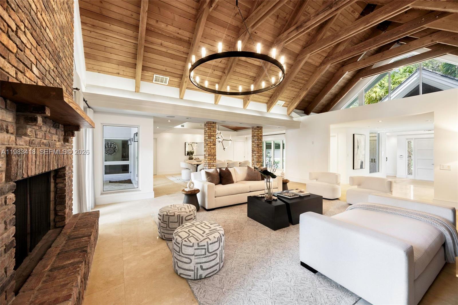 A living room features a vaulted wood-beam ceiling, a brick fireplace, and a large chandelier — 9000 Arvida Dr, Coral Gables FL 33156, CORAL GABLES, FL