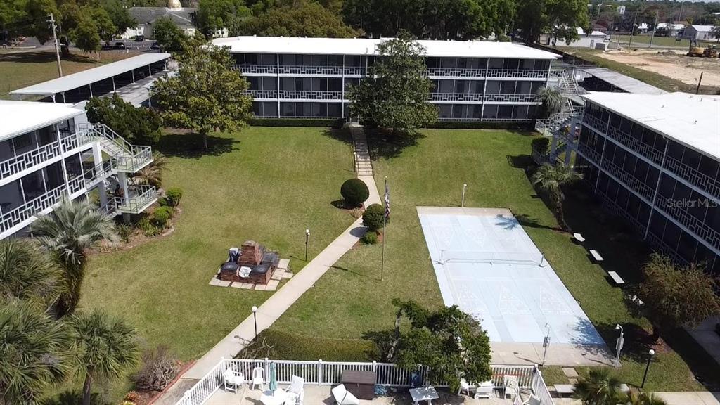 An aerial view shows apartment buildings surrounding a central courtyard with a shuffleboard court — 1700 6TH STREET NW UNIT B23, WINTER HAVEN, FL