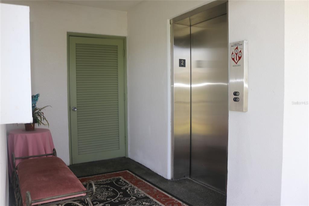 A hallway features a stainless steel elevator, a green louvered door, and a small bench — 1700 6TH STREET NW UNIT B23, WINTER HAVEN, FL