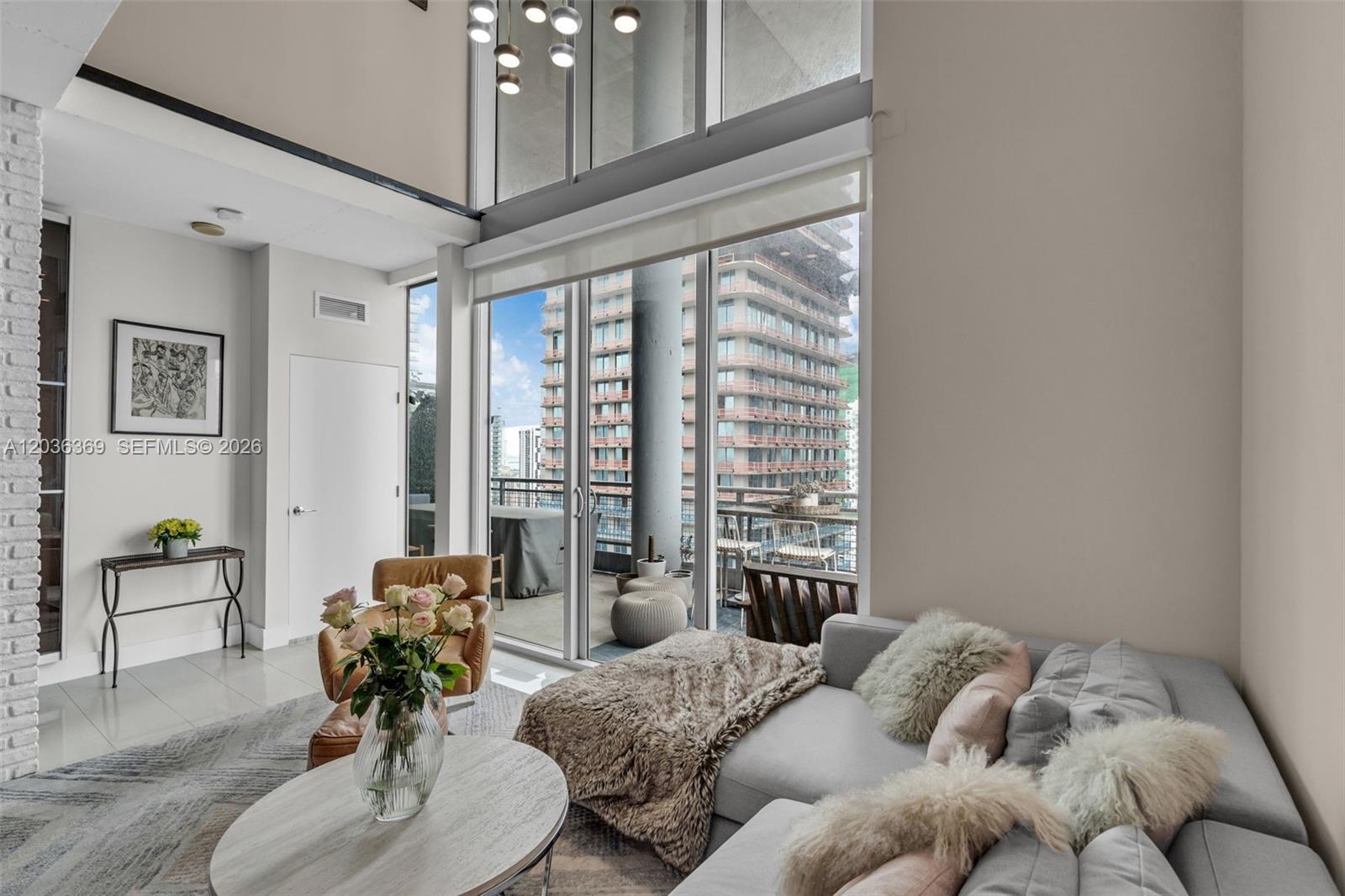 A modern living room features a double-height window wall overlooking a high-rise city balcony — 690 SW 1st Ct, Miami FL 33130, MIAMI, FL