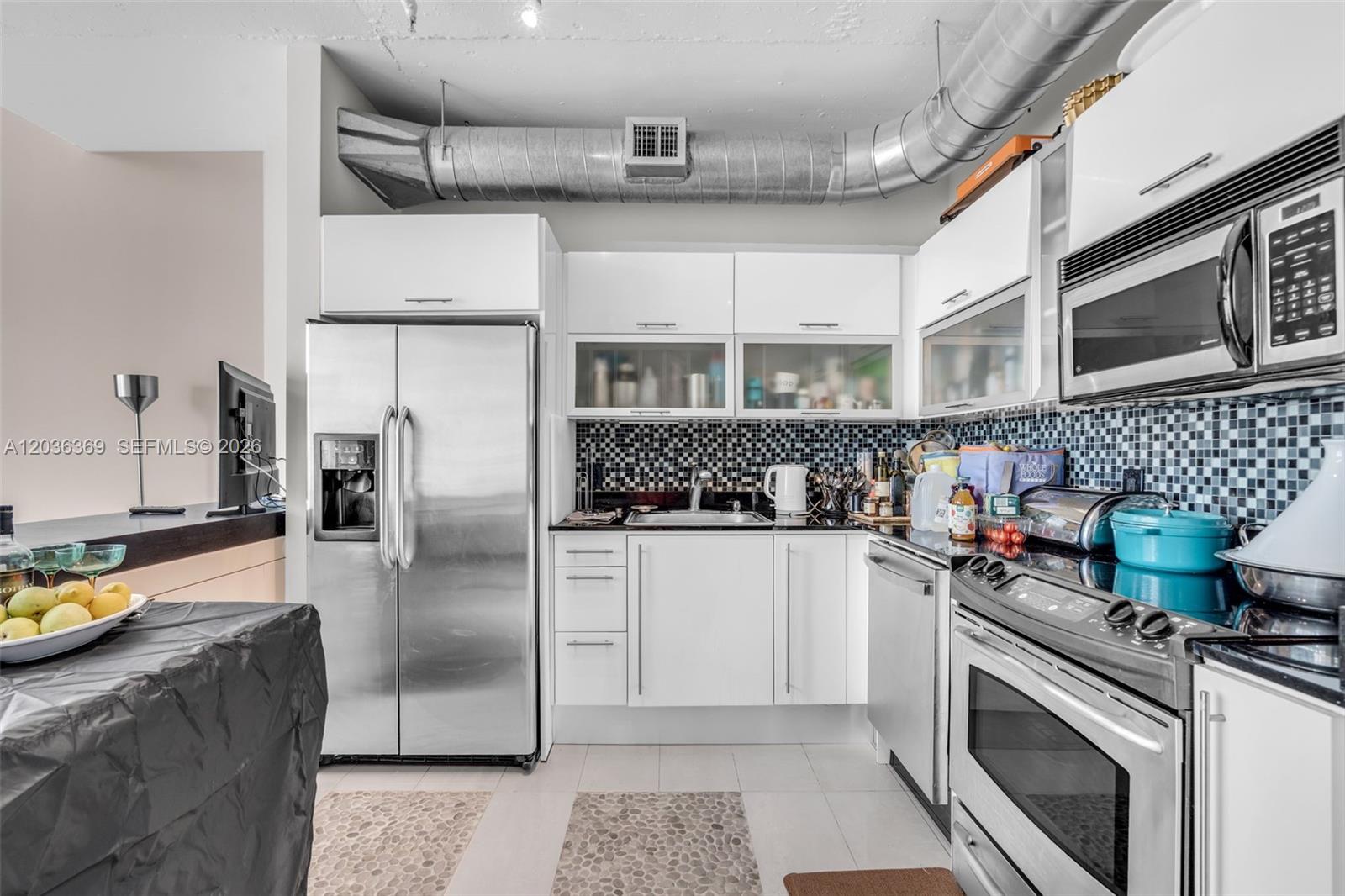 A kitchen features white cabinets, stainless steel appliances, a mosaic backsplash, and exposed ceiling ductwork — 690 SW 1st Ct, Miami FL 33130, MIAMI, FL
