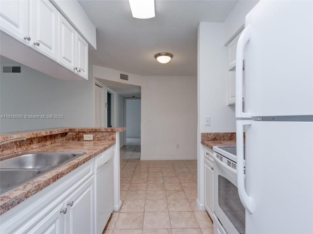 This kitchen features white cabinets, granite countertops, tile flooring, and white appliances — 1235 SW 46th Ave # 707, Pompano Beach FL 33069, POMPANO BEACH, FL